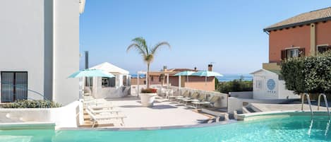 Área de piscina com espreguiçadeiras e guarda-sóis, uma palmeira e vista para o mar.