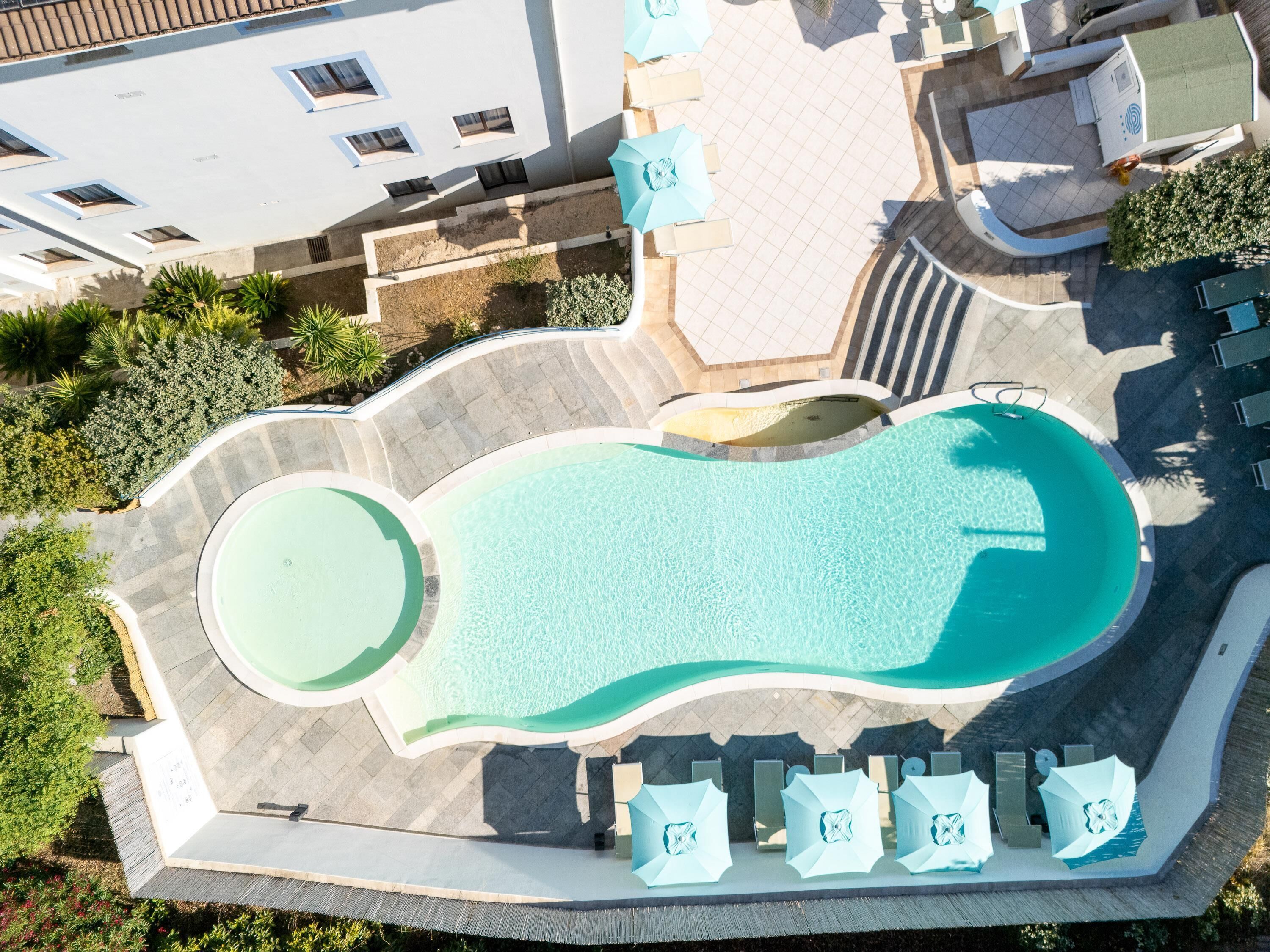 Piscina com borda ondulada, rodeada por espreguiçadeiras e guarda-sóis.