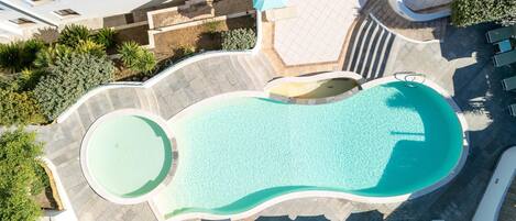 A swimming pool with a wavy edge, surrounded by lounge chairs and umbrellas.