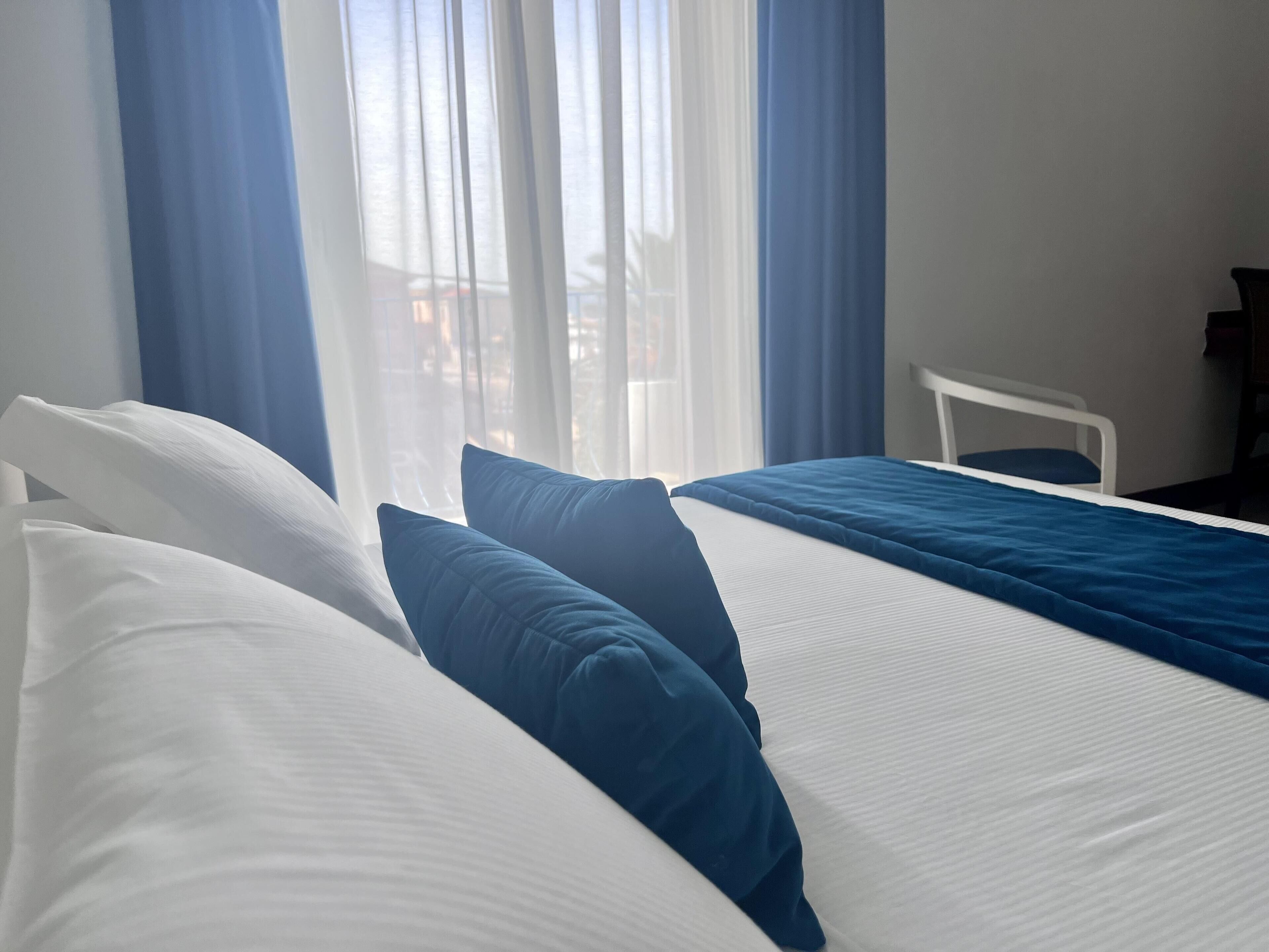 Una habitación de hotel con una cama, una silla y un ventanal con cortinas.
