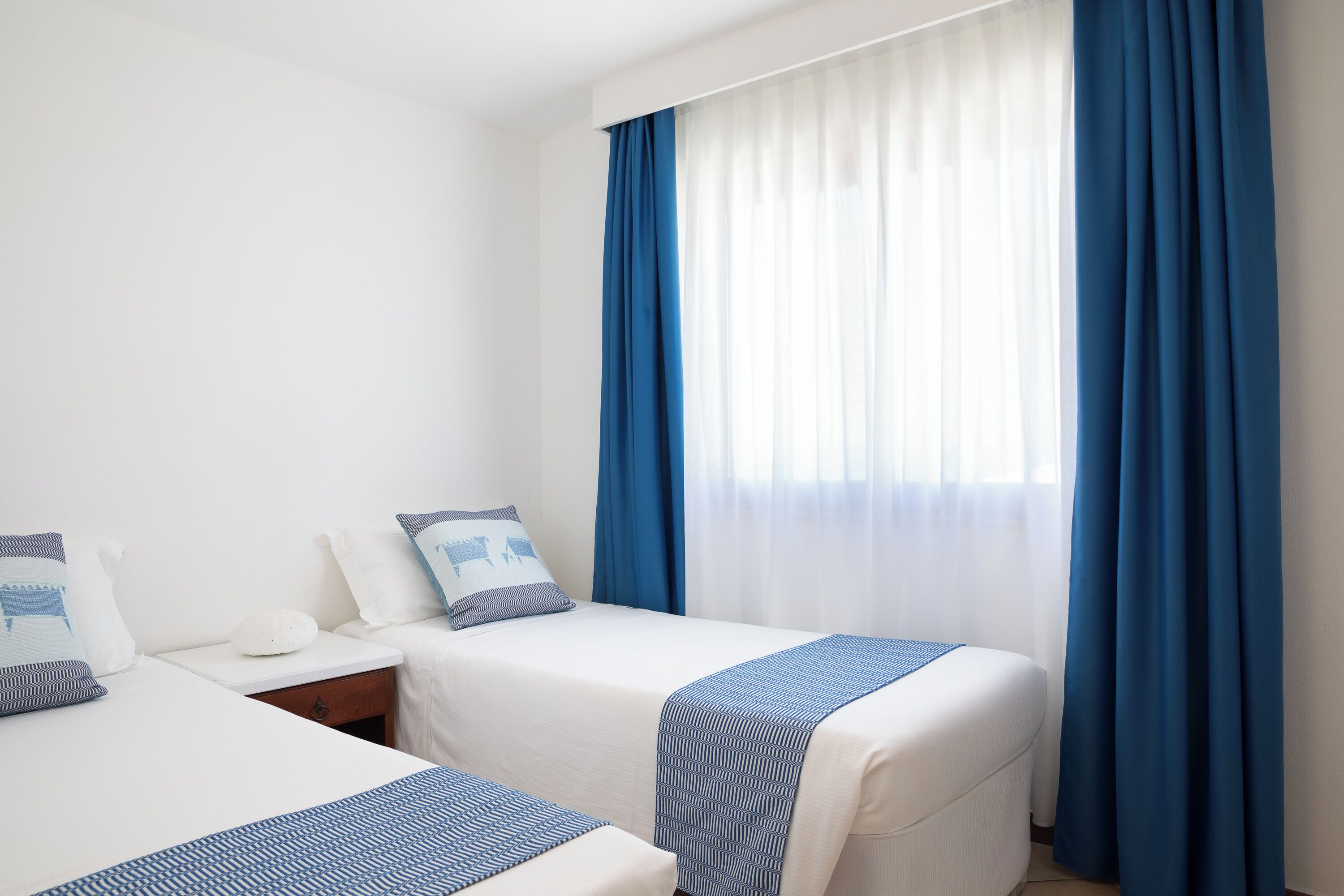 Ein Hotelzimmer mit zwei Betten, einem Nachttisch und einem Fenster mit blauen Vorhängen.