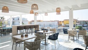 A spacious outdoor seating area with wicker furniture and hanging rattan lamps, overlooking a cityscape. - Hotel Blumarea, BW Signature Collection (Castelsardo)