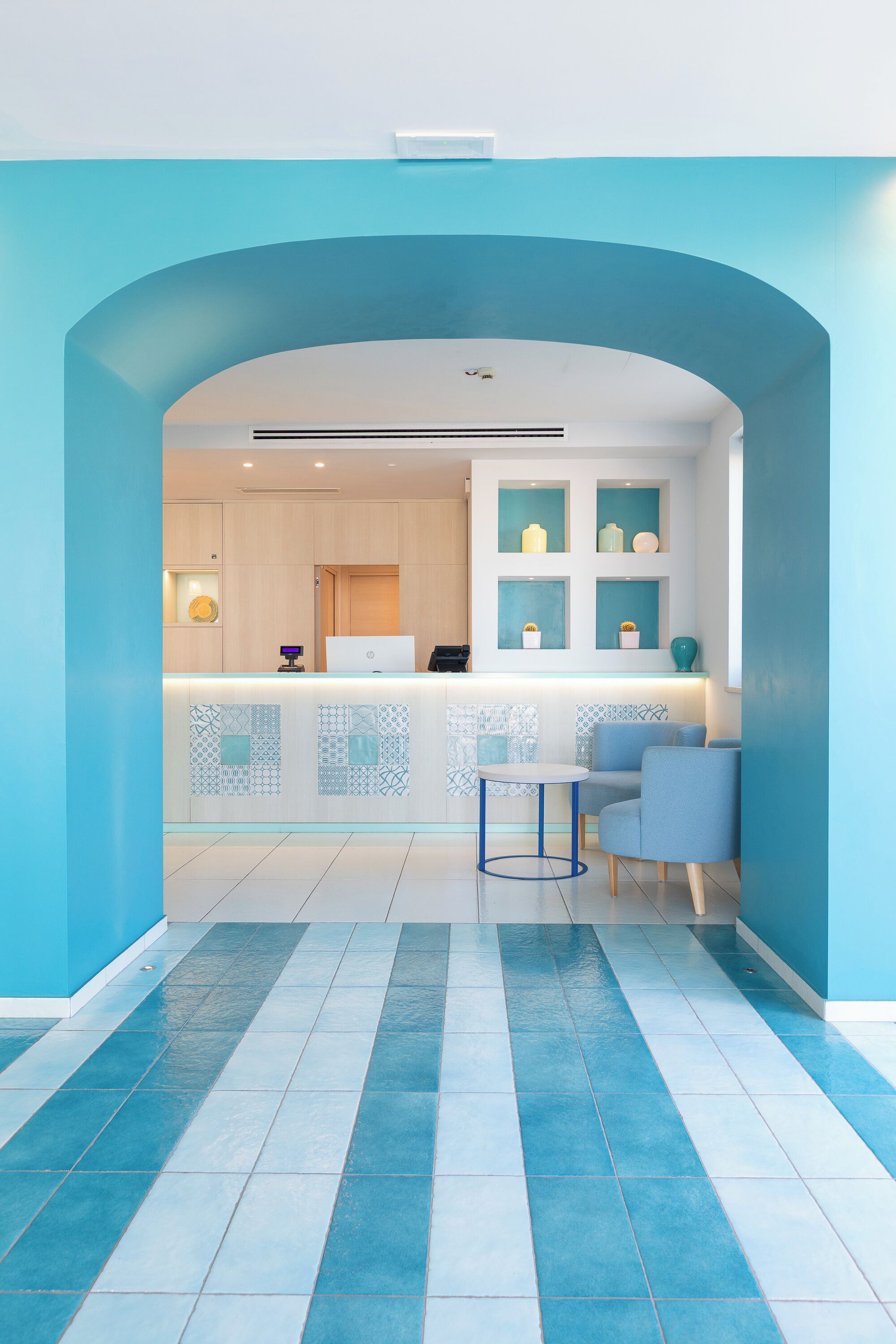 Un espace d’accueil moderne avec un comptoir blanc, des carreaux aux motifs bleus et blancs, et une palette de couleurs bleue et blanche.