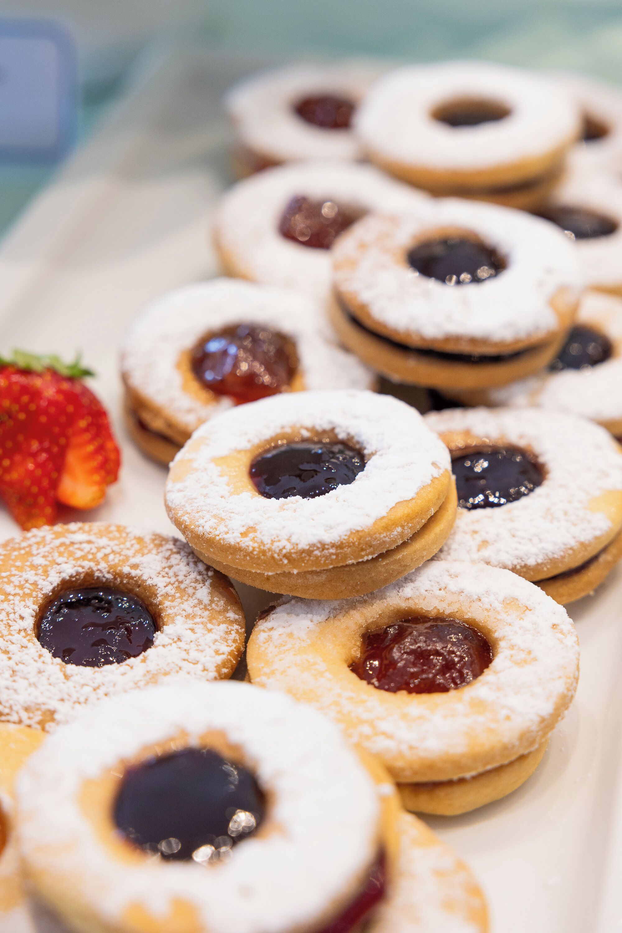 A tray of round pastries with a jam filling, dusted with powdered sugar, and a whole strawberry on the side.