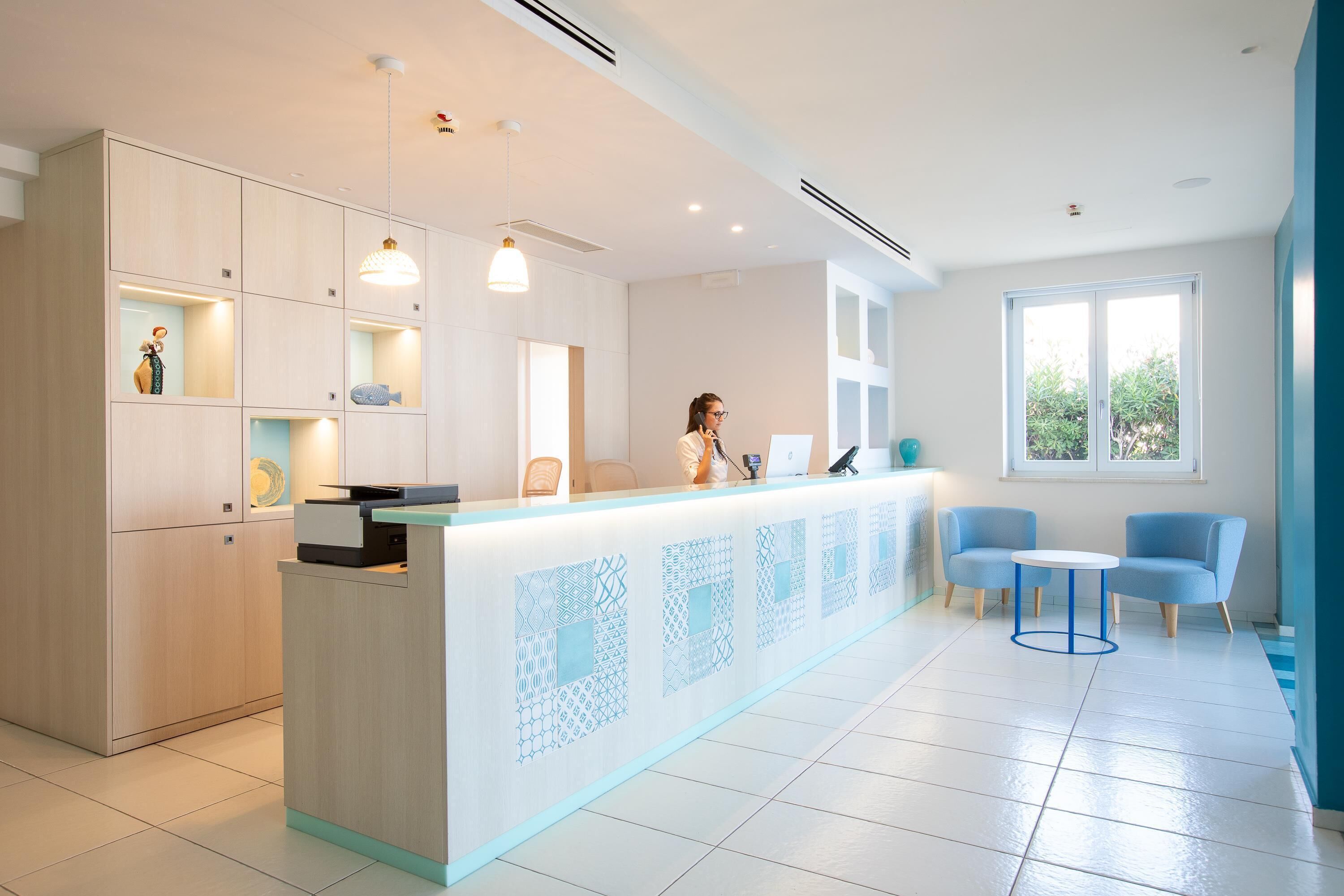 A modern reception area with a light-colored counter, blue chairs, and a large window providing natural light.