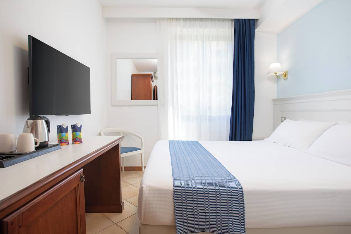 Camera d'albergo con un letto, una scrivania con televisore, una macchina per il caffè e una sedia.