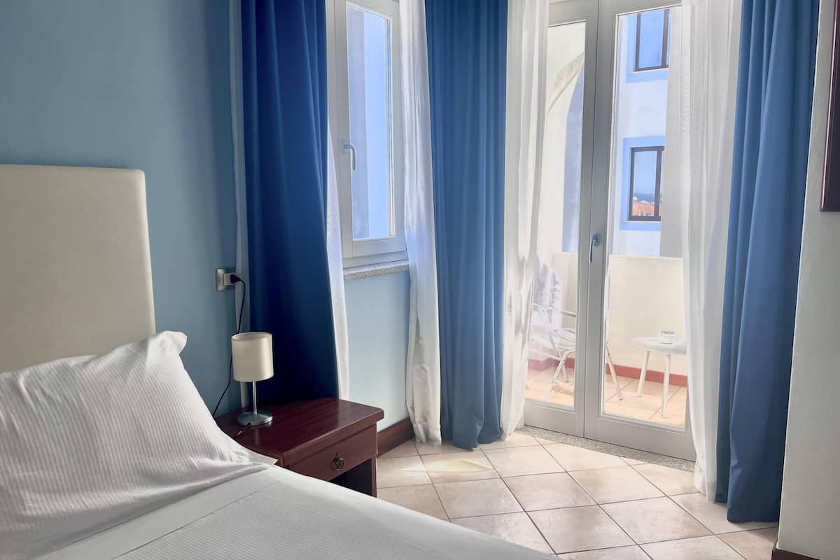 Una camera d'albergo con un letto, un comodino, una lampada e vista sul balcone esterno.