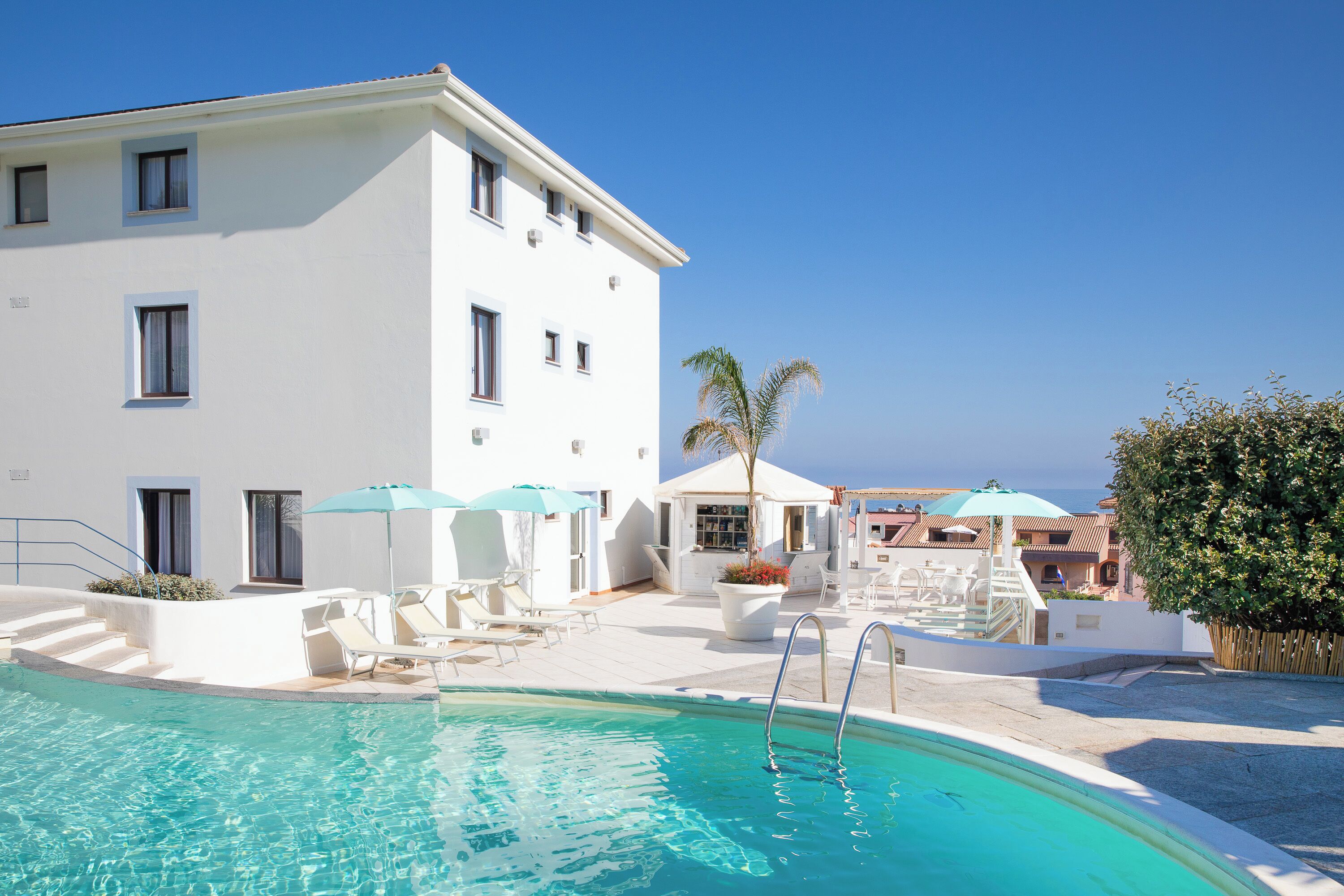 Un edificio blanco con piscina, mobiliario exterior y una palmera.