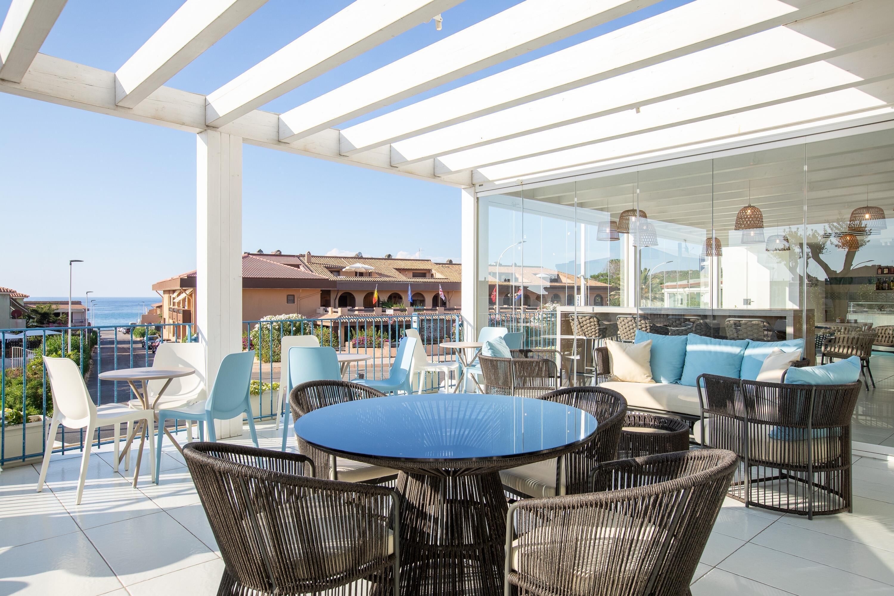Eine Terrasse im Freien mit Korbmöbeln, einem runden Tisch und einem mit Kissen ausgestatteten, verglasten Bereich.