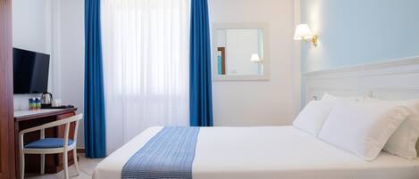 Une chambre d’hôtel équipée d’un lit, d’un bureau, d’une chaise, d’une télévision et d’une fenêtre avec des rideaux.
