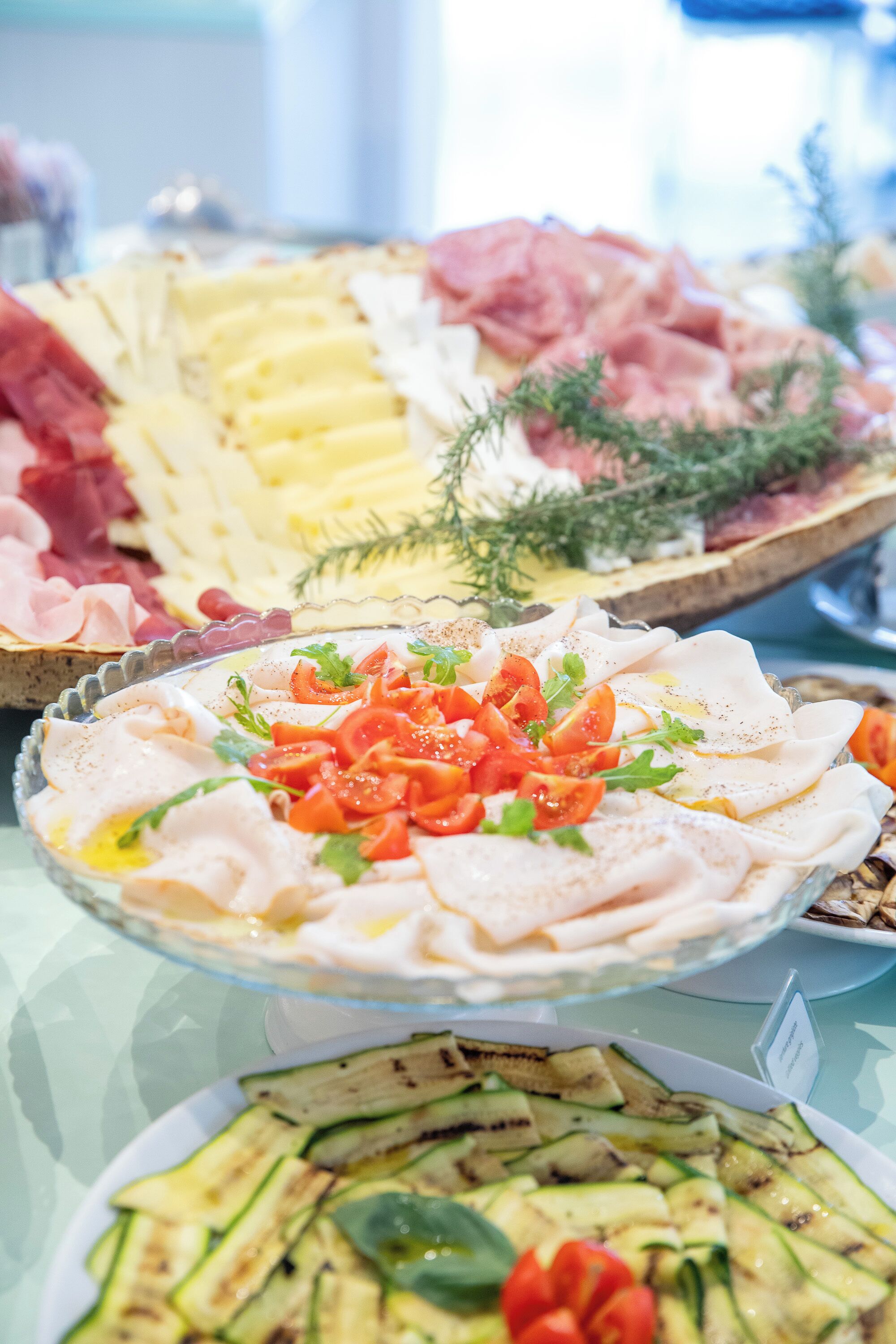 A buffet with various food items including sliced meats, cheeses, and a salad with tomatoes and greens.