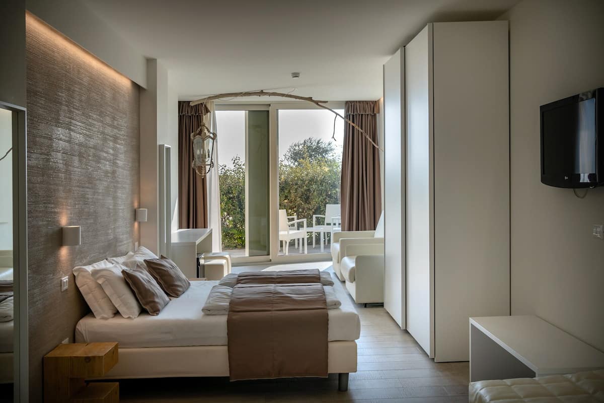A modern bedroom with a large bed, a TV mounted on the wall, and a view of the outdoors through the window.