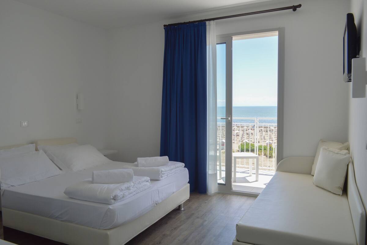 A hotel room with a bed, a sofa, and a balcony with a view of the sea.