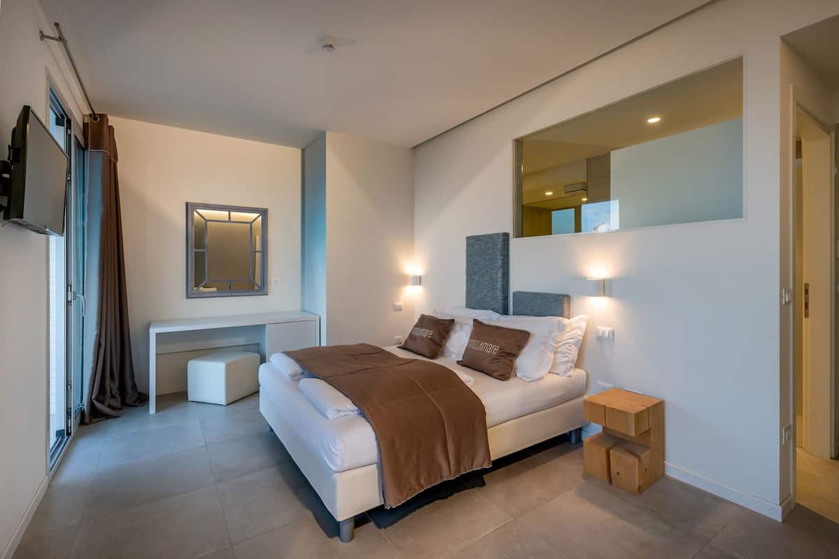 A modern bedroom with a bed, bedside tables, a desk, and a mirror.