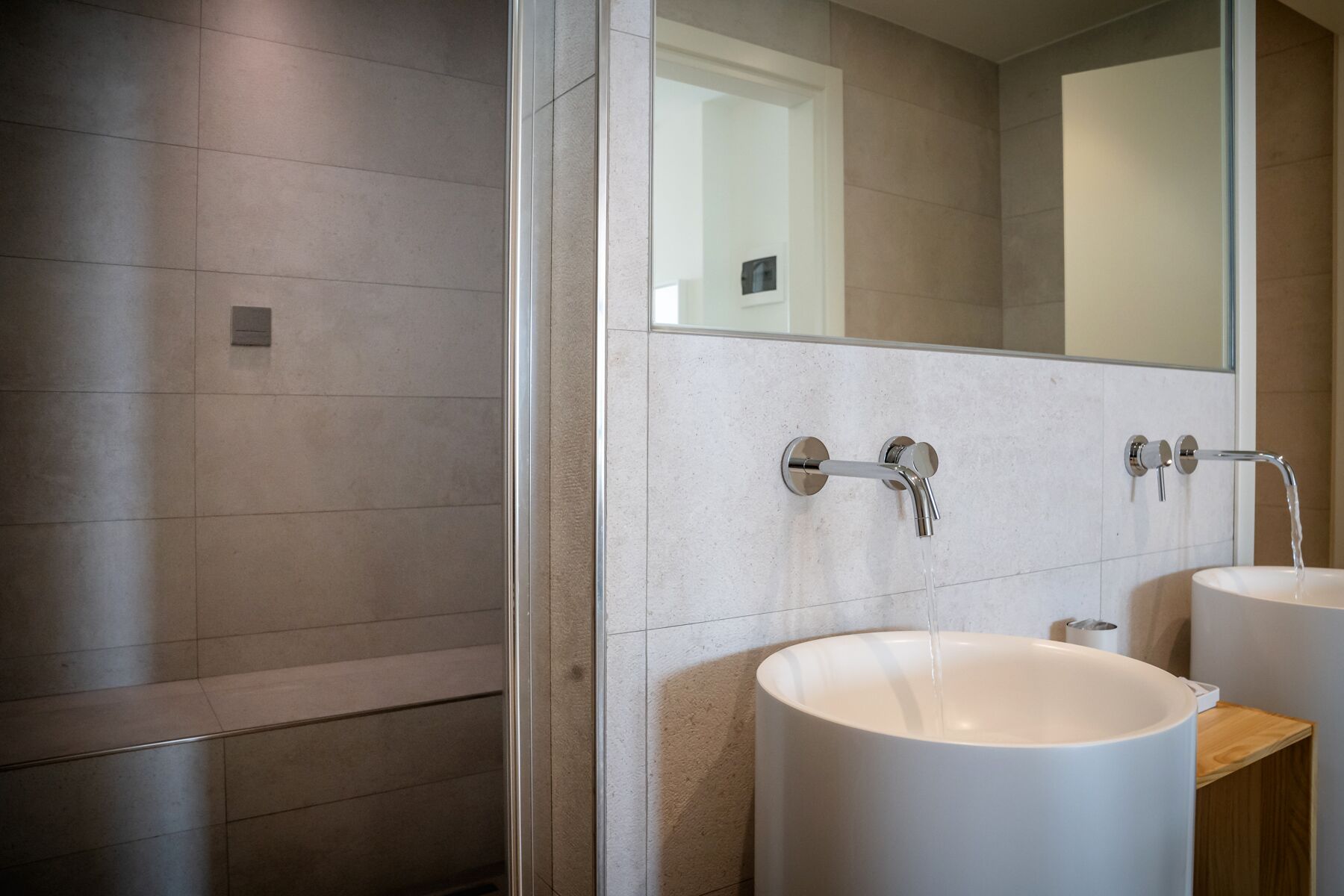 A modern bathroom with two sinks, a glass shower enclosure, and a large mirror.