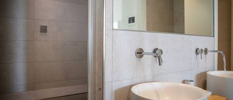 A modern bathroom with two sinks, a glass shower enclosure, and a large mirror.