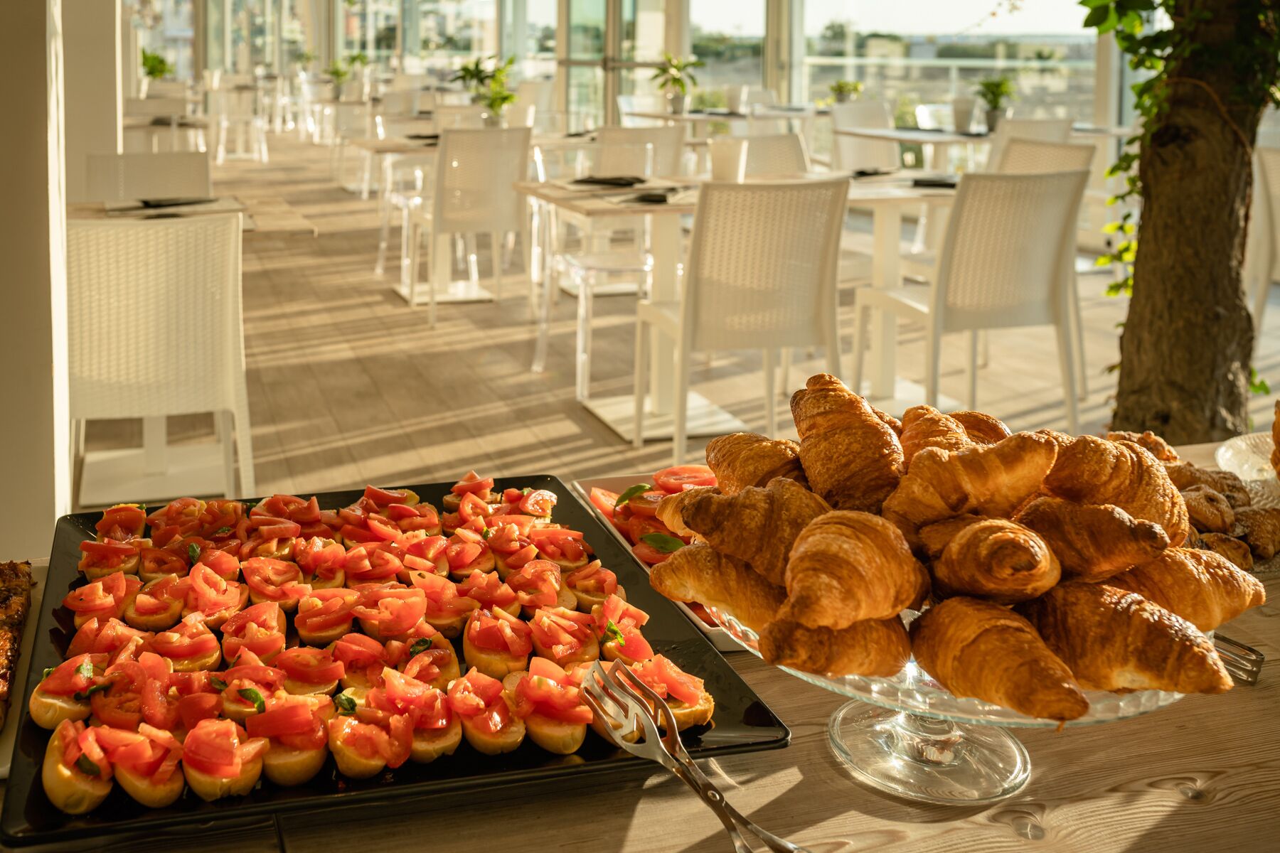 A buffet table with croissants and a dish of tomato-based appetizers.