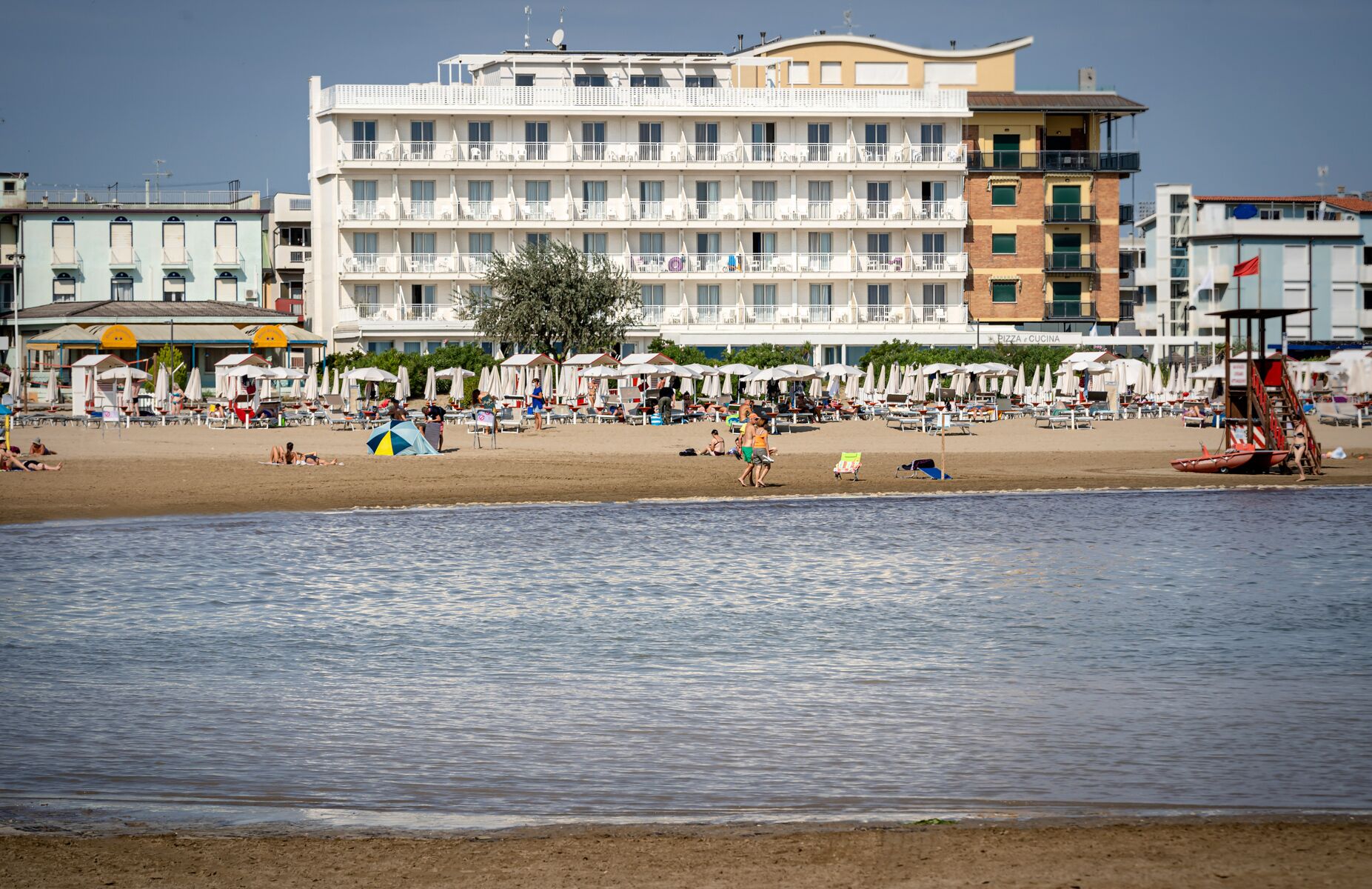 A beachfront hotel with multiple balconies, beach umbrellas, and a lifeguard tower.
