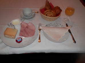 A breakfast setting with a plate of ham, cheese, and croissants, a cup of coffee, and a glass of orange juice. - Château Ardilleux (Valdelaume)