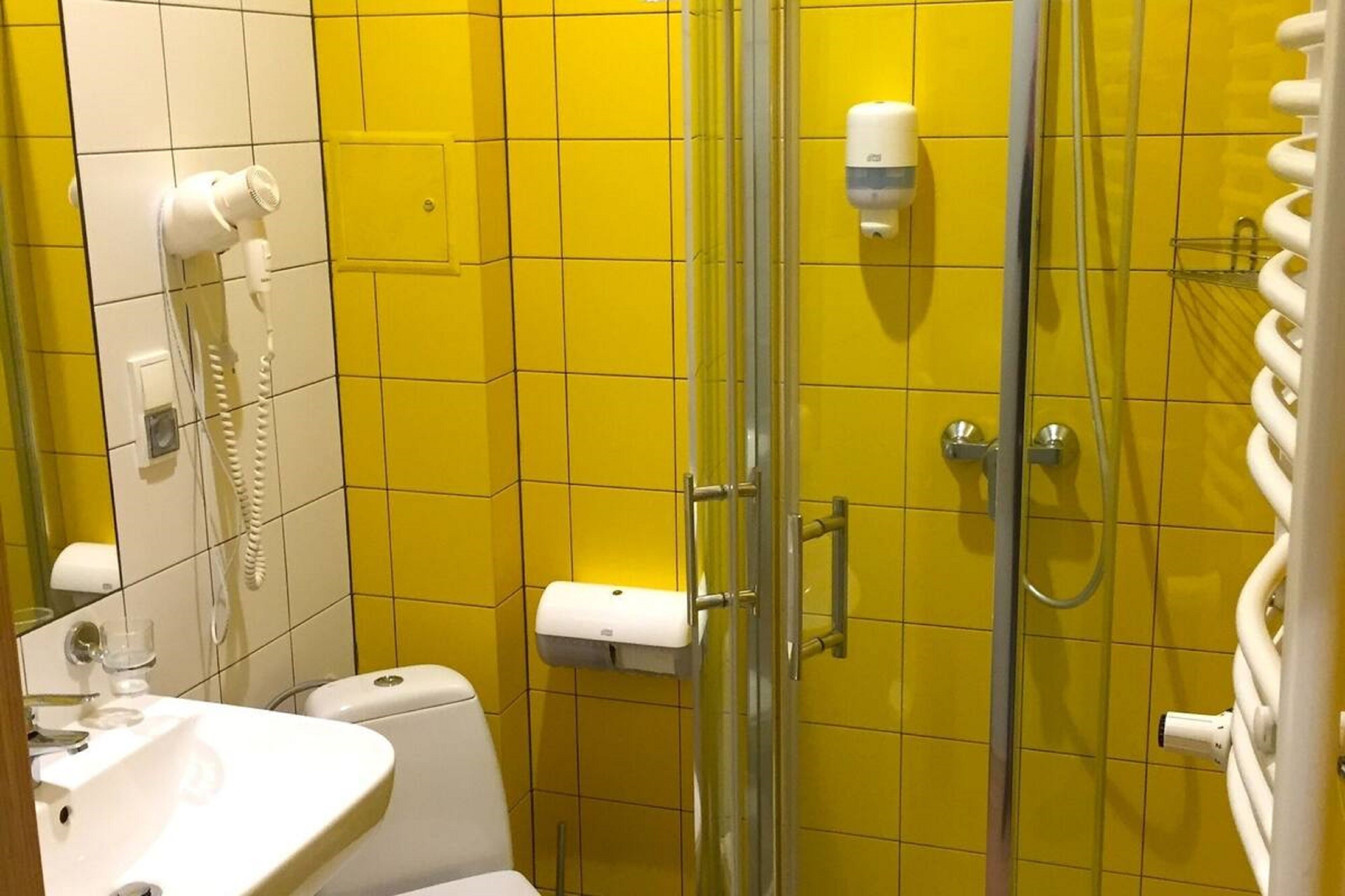 A bathroom with yellow tiles, a white sink, a toilet, a glass shower enclosure, and a hand dryer.