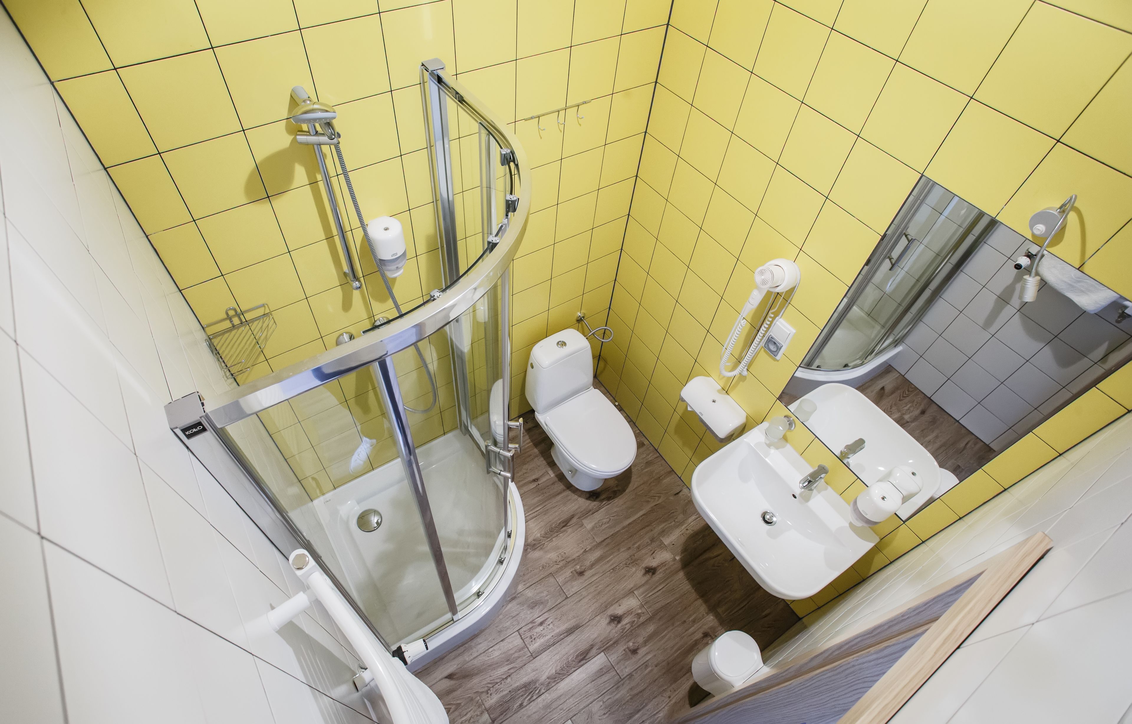 A bathroom with yellow tiles, a glass-enclosed shower, a toilet, and a sink.