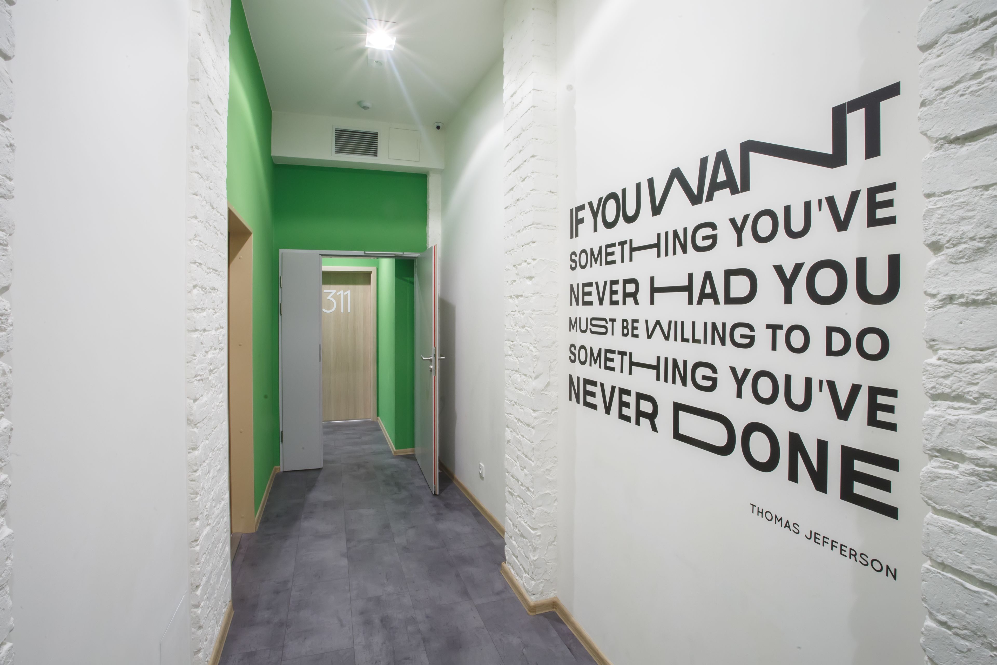 Un pasillo con una cita motivacional en la pared, una puerta con la etiqueta “311” y una decoración en tonos verde y blanco.