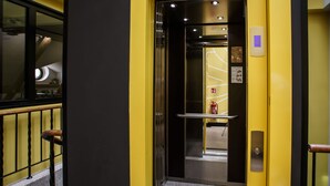 Un ascensor con interior metálico, un extintor de incendios en la pared y un pequeño ventanuilla en la parte superior.
