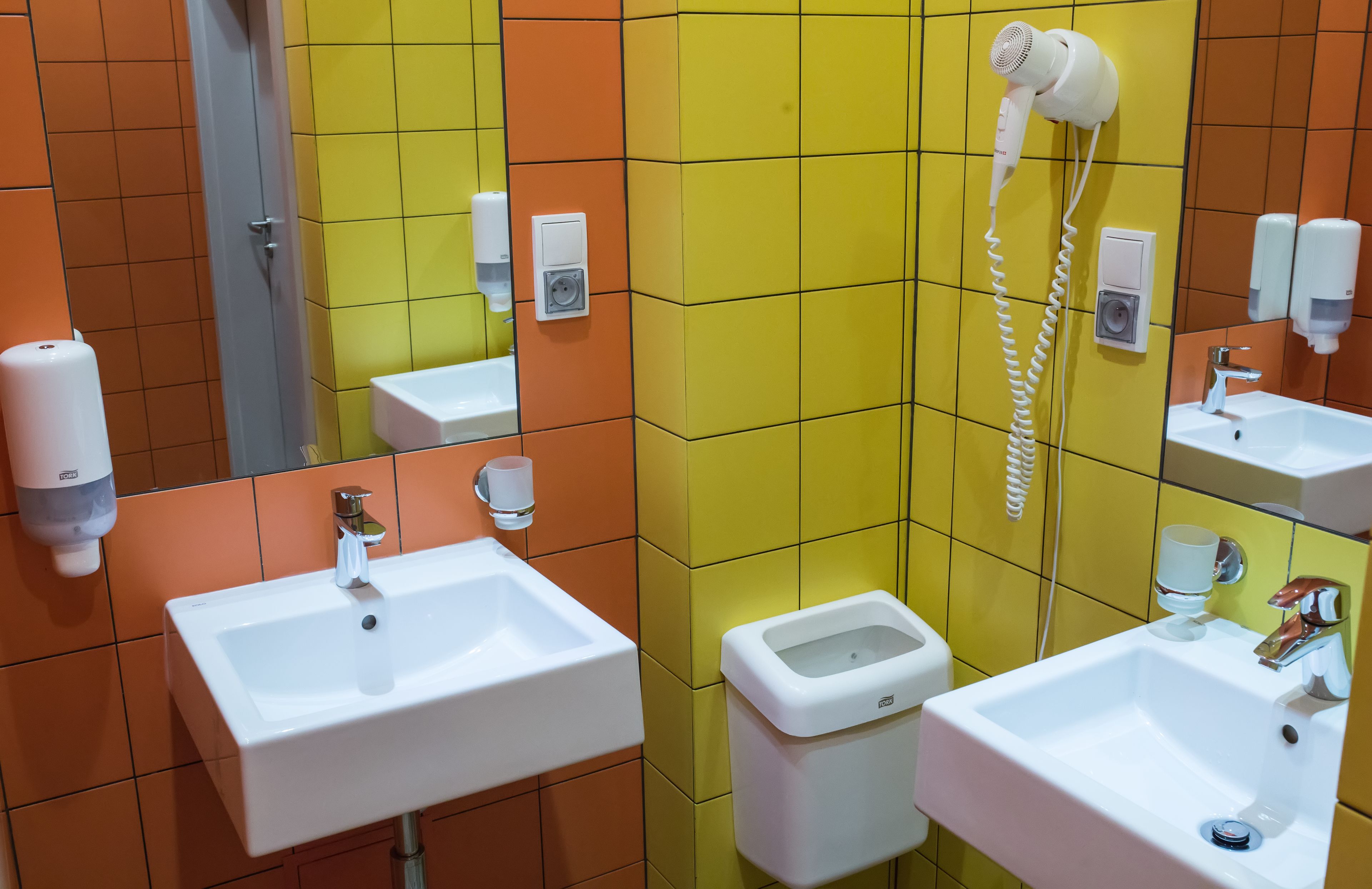 A bathroom with multiple sinks, a hairdryer, and hand soap dispensers.