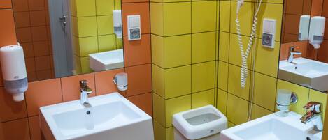 Un baño con varios lavamanos, un secador de pelo y dispensadores de jabón para manos.