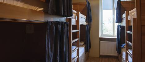 A dormitory room with bunk beds, a window, and a radiator.