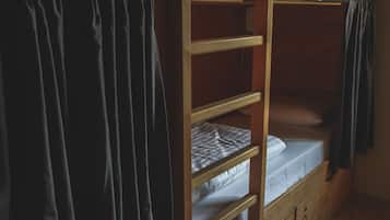 A bunk bed with a wooden frame, a white mattress, and a dark curtain.