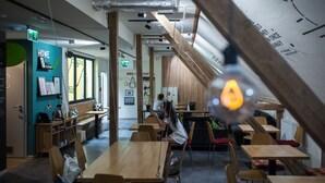 Un interior moderno con mesas y sillas de madera, un letrero que dice 'HOME' y una persona usando una computadora portátil.