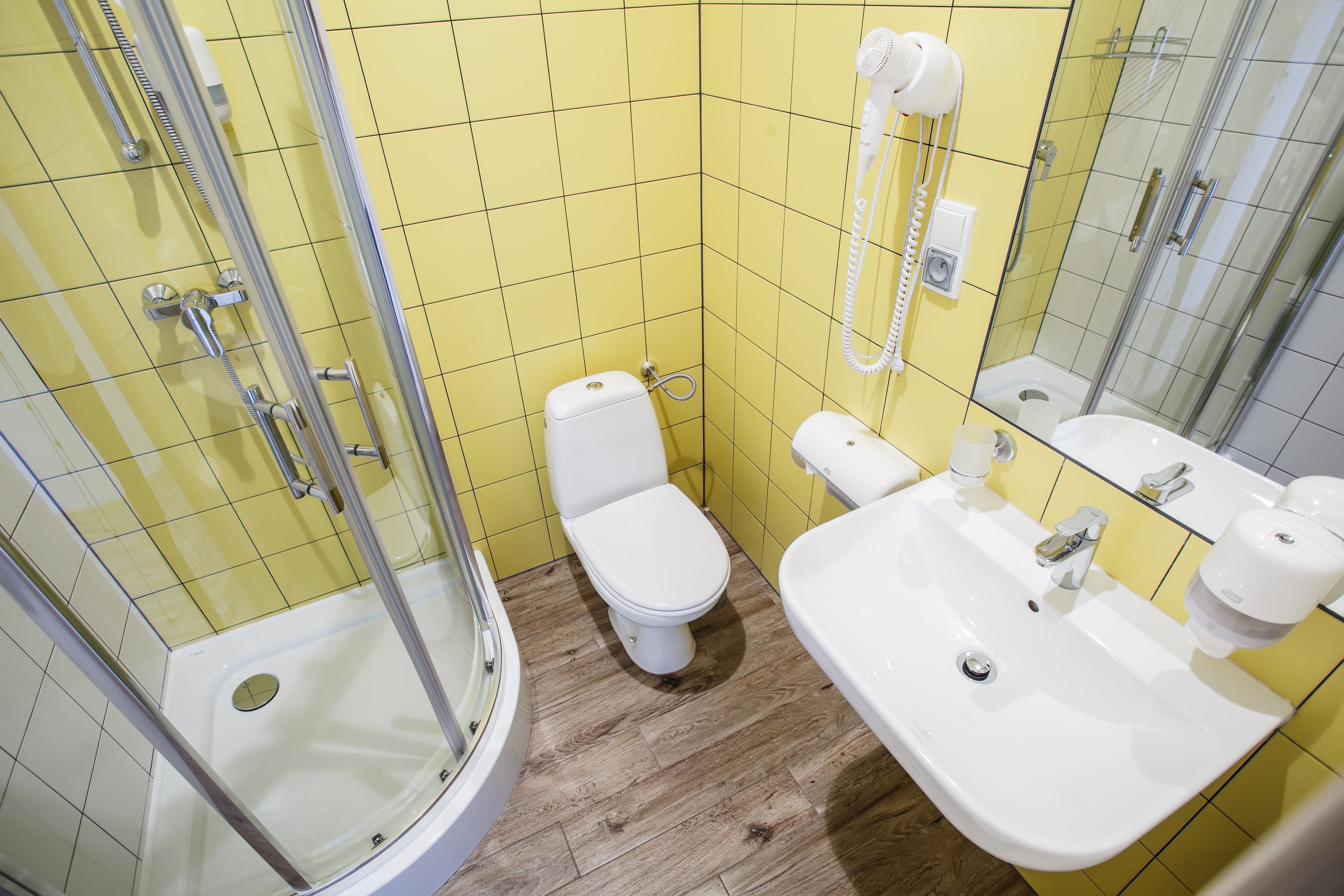 A bathroom with yellow tiles, a white toilet, a sink, and a shower.