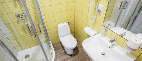 A bathroom with yellow tiles, a white toilet, a sink, and a shower.