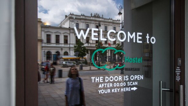 Letrero de bienvenida para un hostal con vistas a un edificio histórico al fondo.