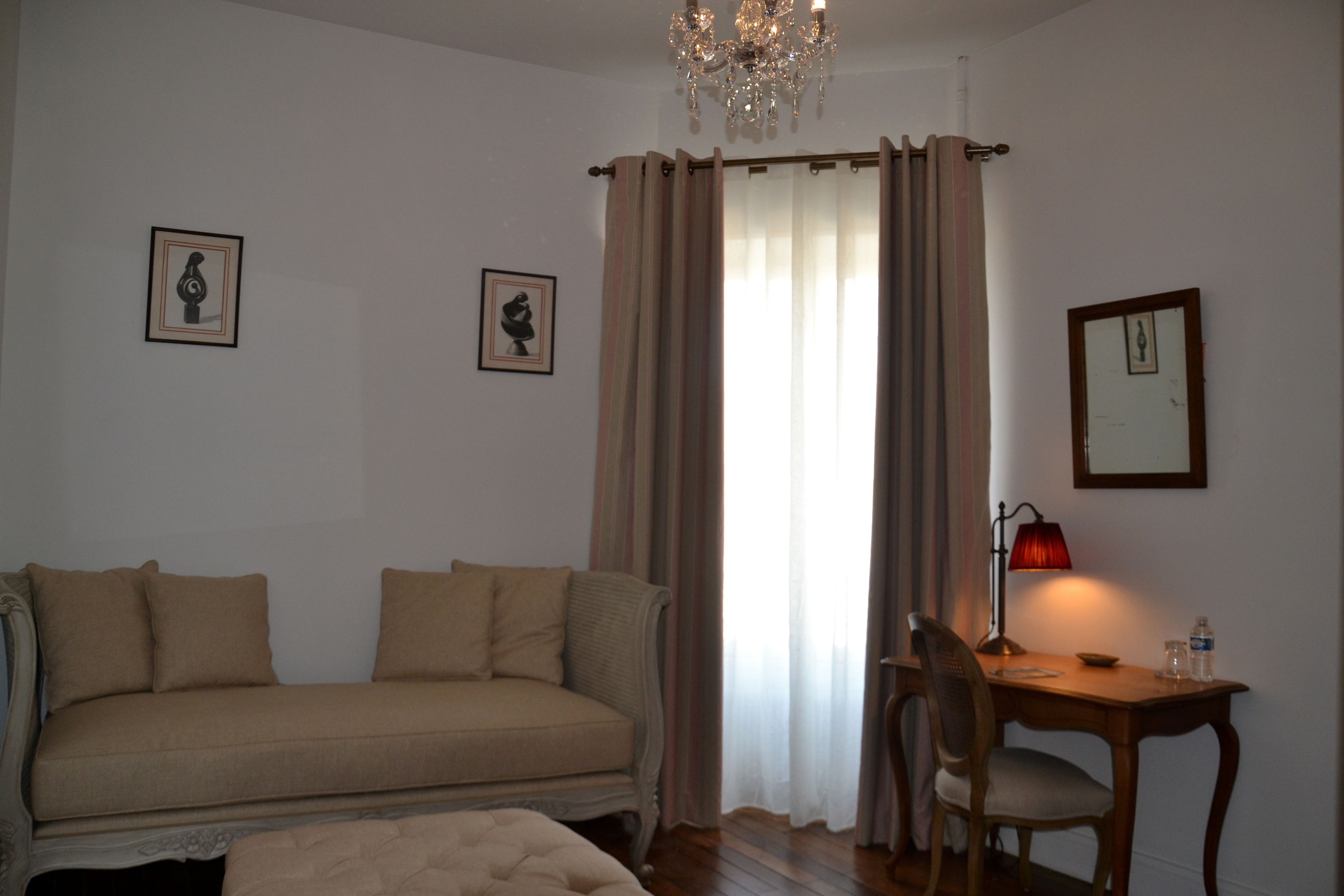 A room with a sofa, a wooden table with a chair, a lamp, and a chandelier.
