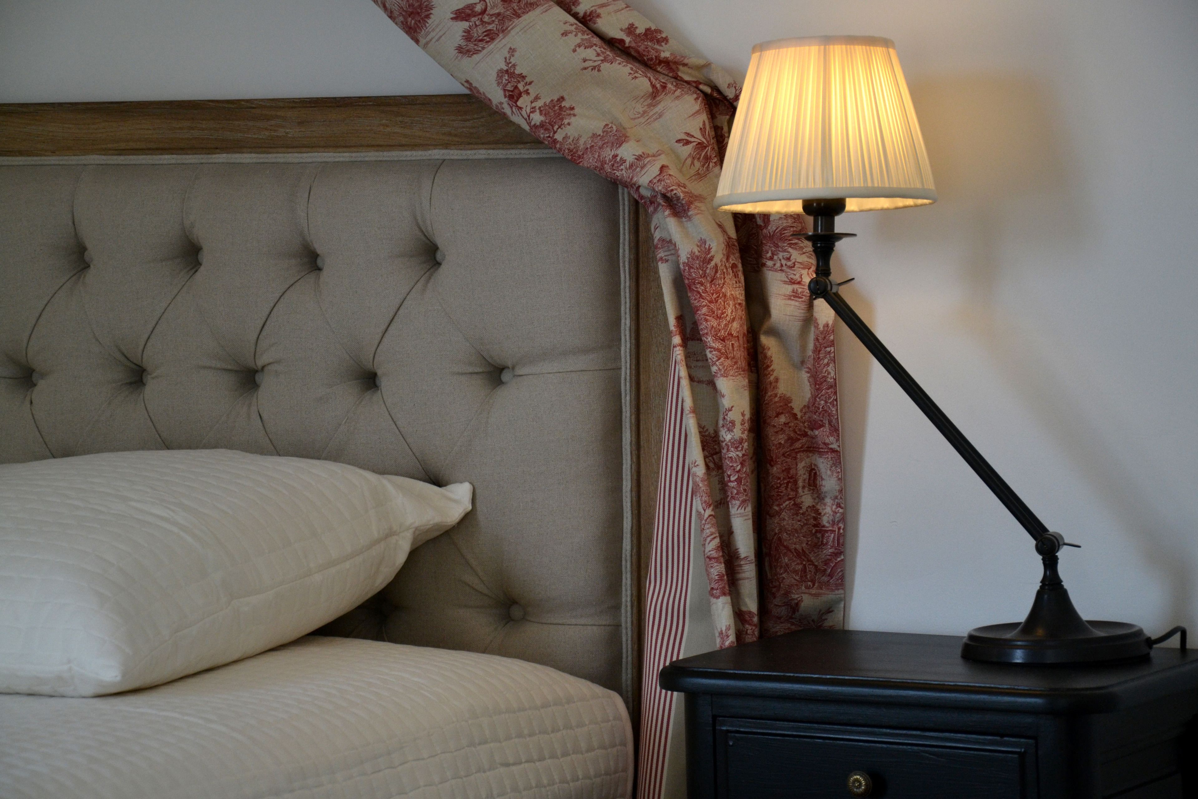 A bedroom with a tufted headboard, a bedside lamp, and a nightstand.