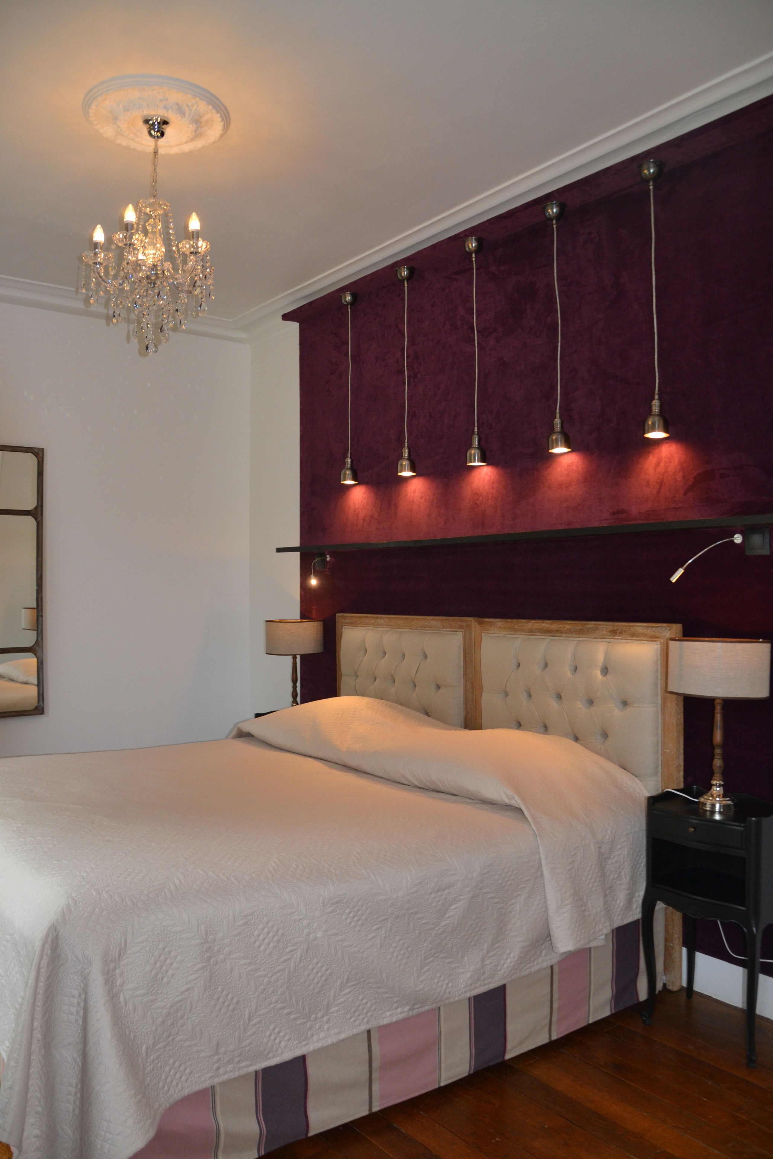 A bedroom with a large bed, a chandelier, and a red accent wall.