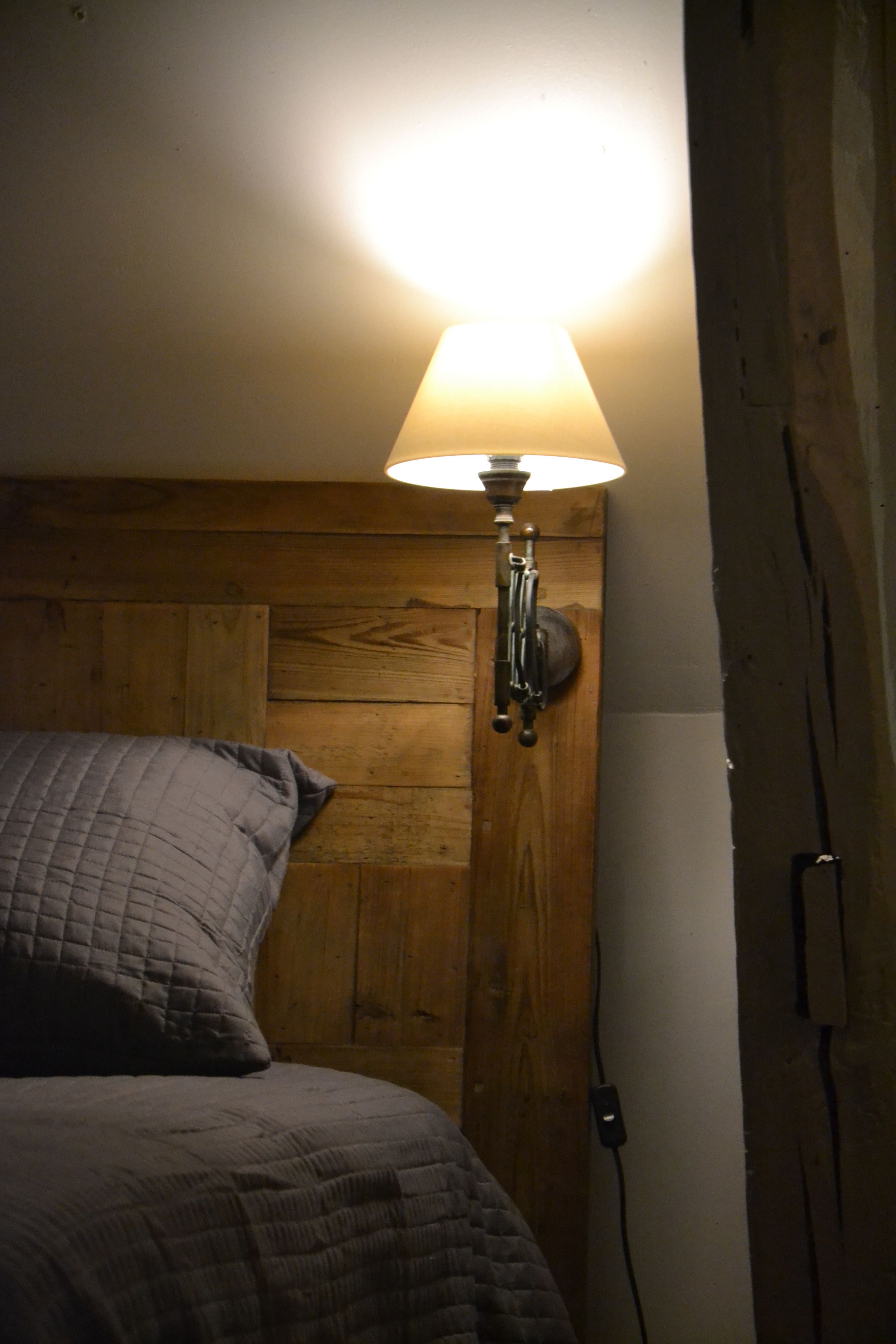 Un lit avec une tête de lit en bois, une lampe fixée au mur et une prise de courant.