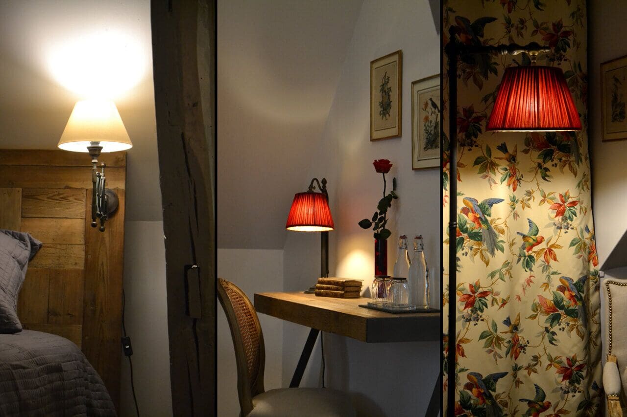 A room with a wooden door, a bed, a desk with a lamp, and a floral wallpaper.