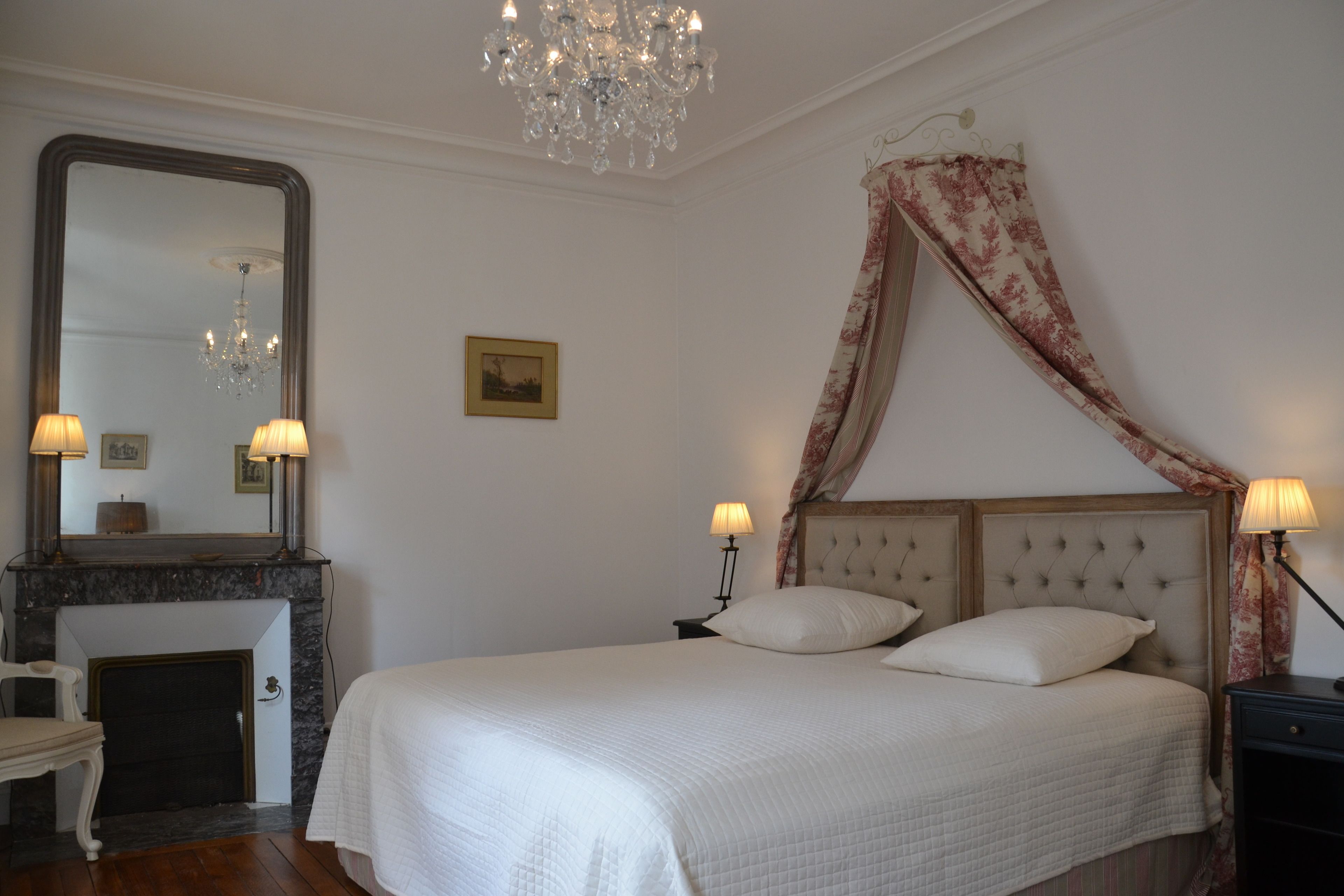 A bedroom with a large bed, a chandelier, a fireplace, and a mirror.