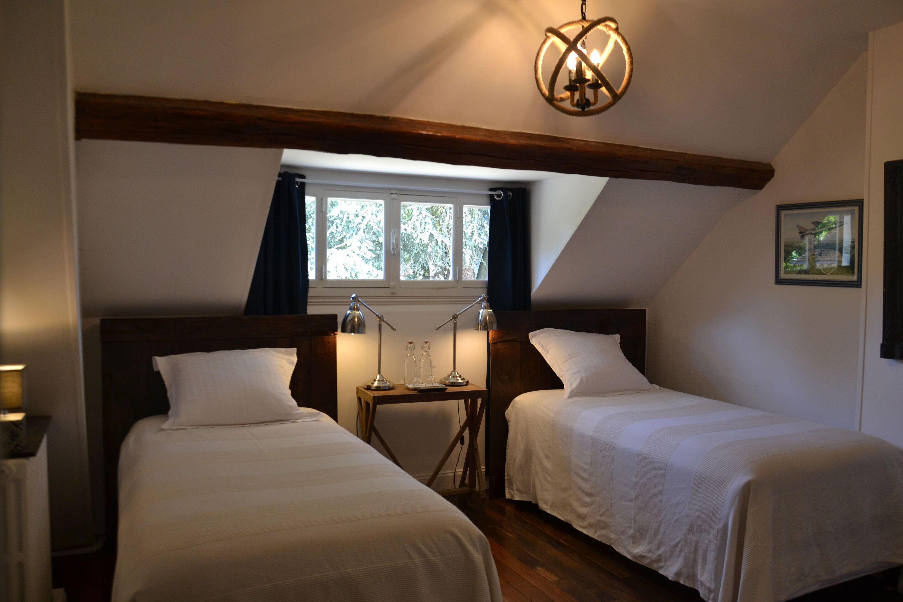 Ein Zimmer mit zwei Betten, einem Fenster mit Vorhängen, einem Tisch mit Lampen und einer Kandelaber.