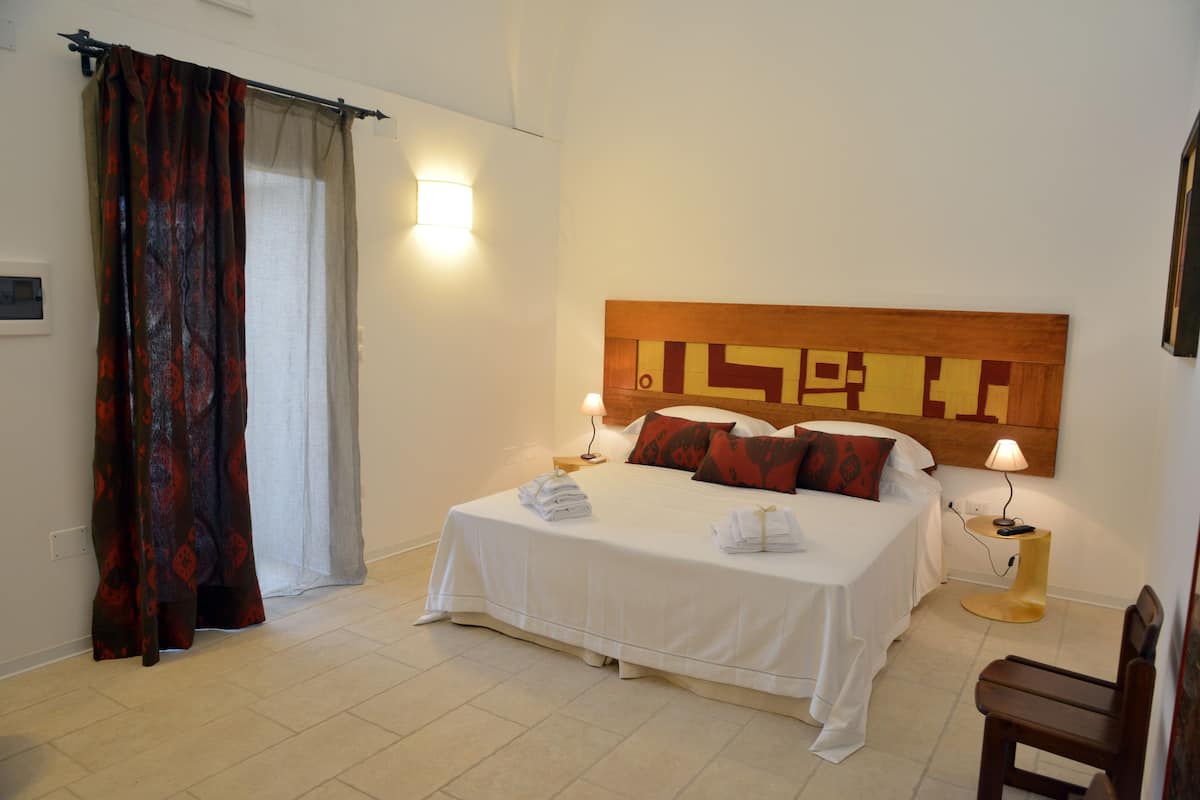 Un cuarto de hotel con una cama grande, dos mesitas de noche con lámparas, un cabecero de madera y una cortina en la ventana.
