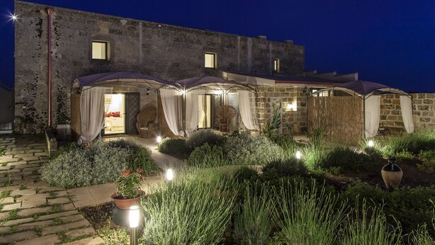 A stone building with a garden entrance, potted plants, and outdoor seating areas. - Masseria Palane (Patu)