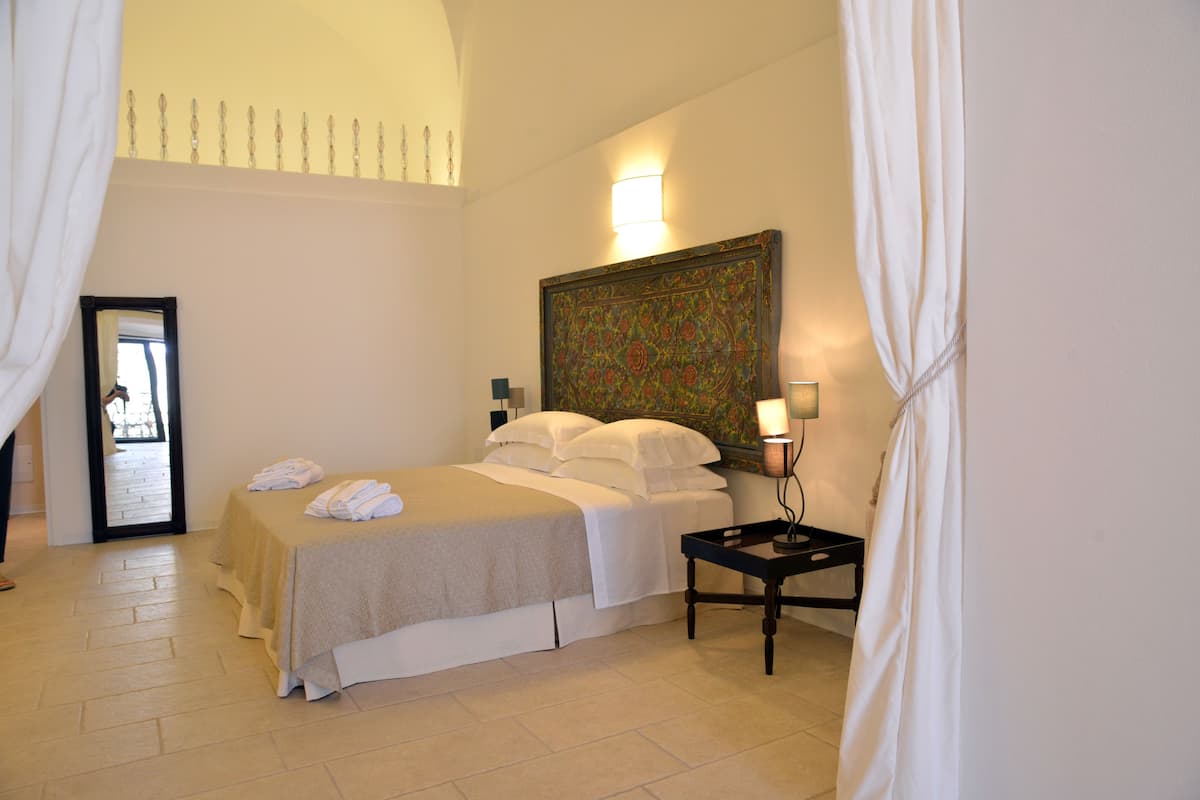 Una habitación de hotel con cama, mesita de noche, lámpara y un cuadro en la pared.