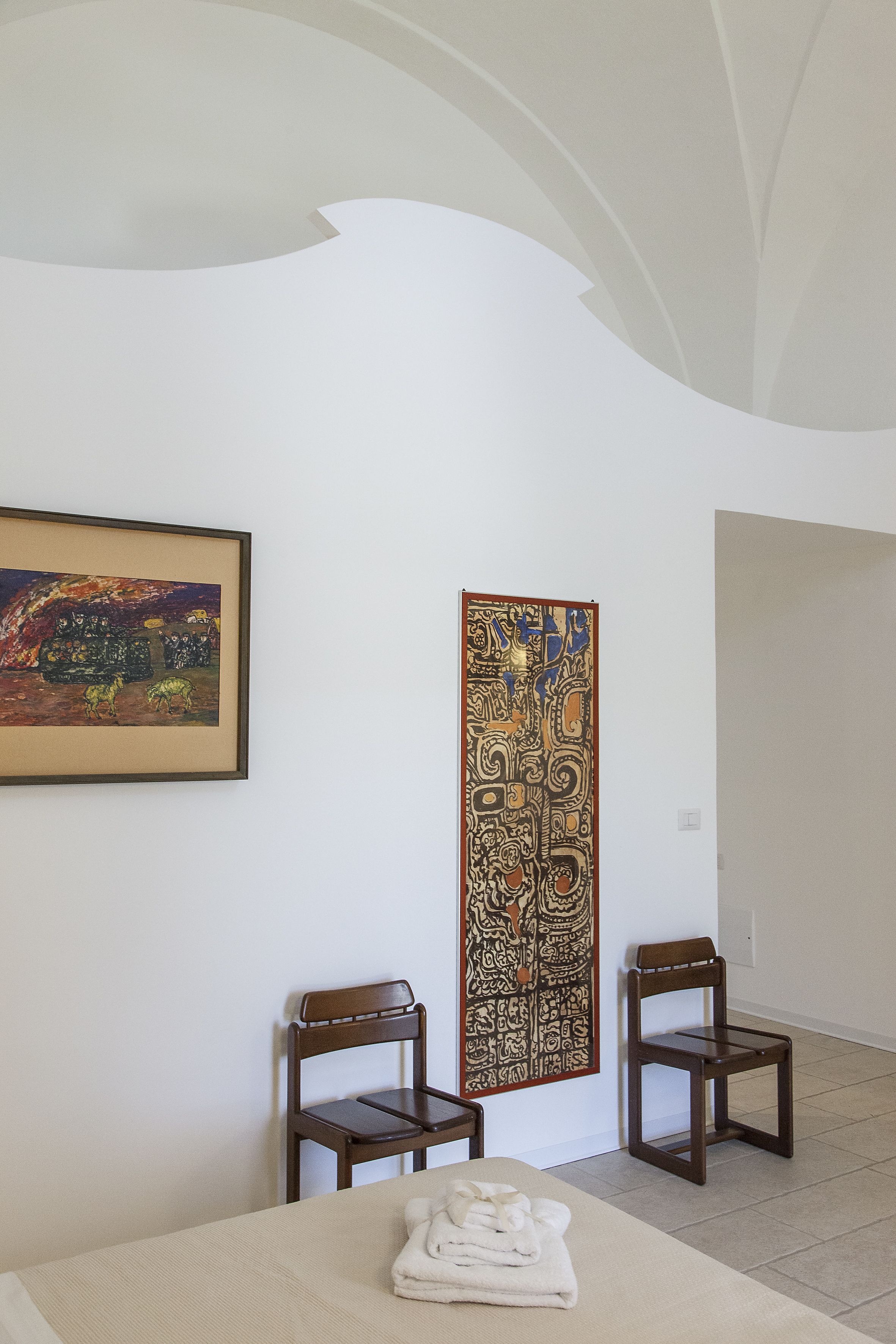 A room with a bed, two chairs, a painting, and a decorative panel.