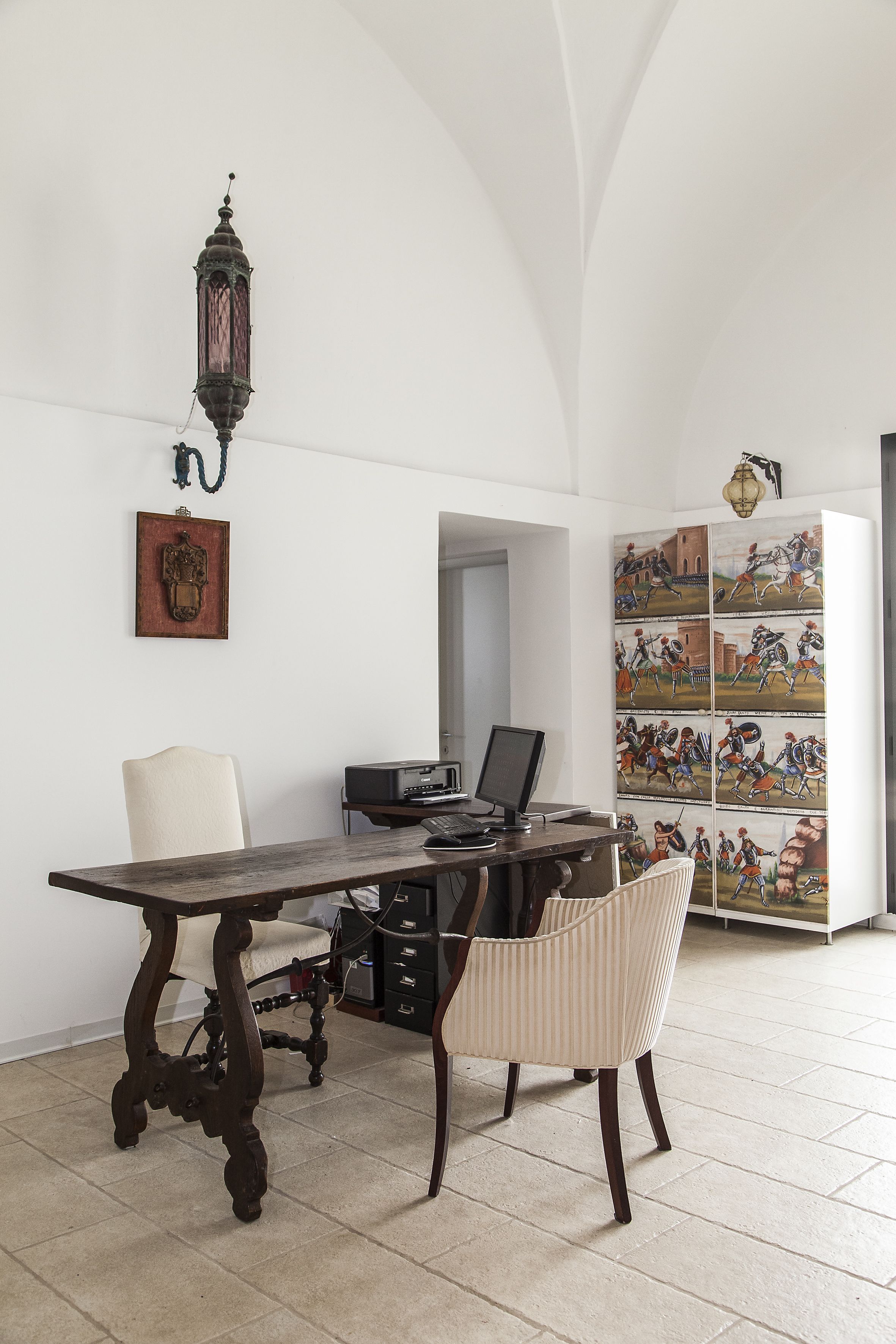 Una habitación con un escritorio de madera, una computadora, una silla y un estante de pared con fotografías enmarcadas.