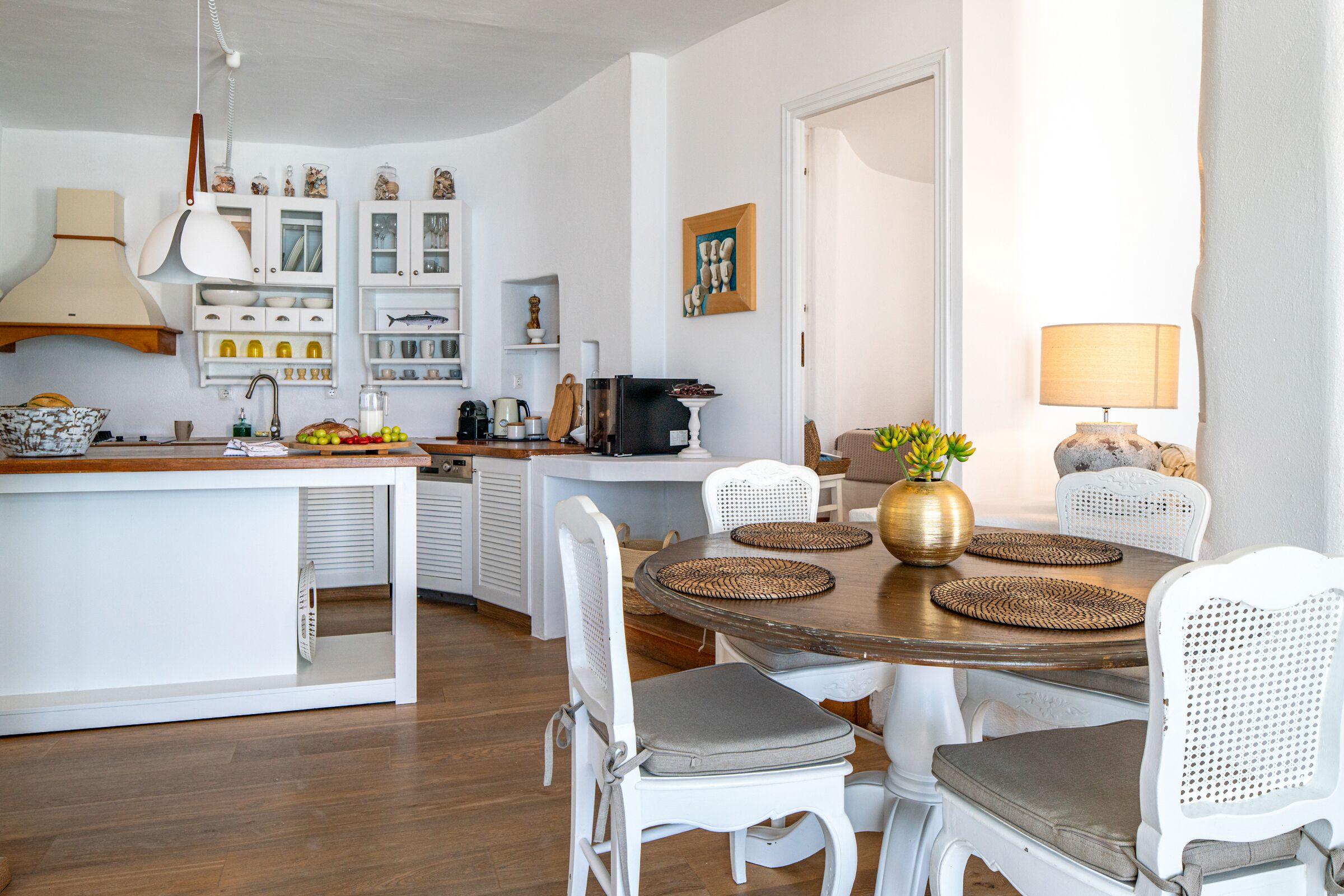A modern kitchen with white cabinetry, a central island, and a dining area with a round table and white chairs.