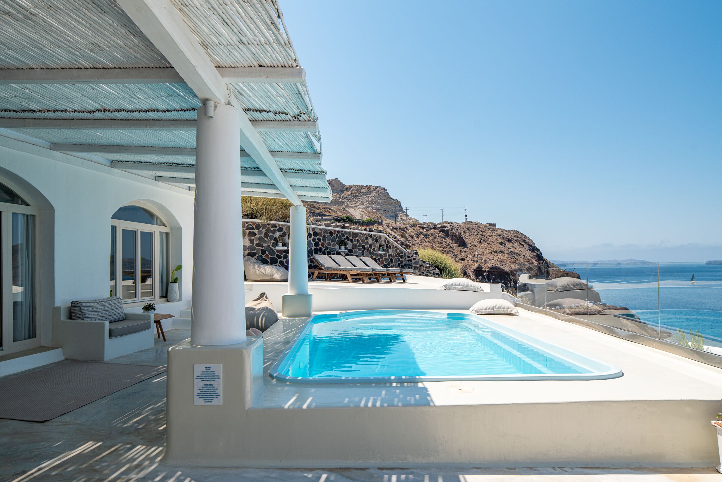 A pool area with a view of the ocean, a lounge chair, and a rocky hillside.