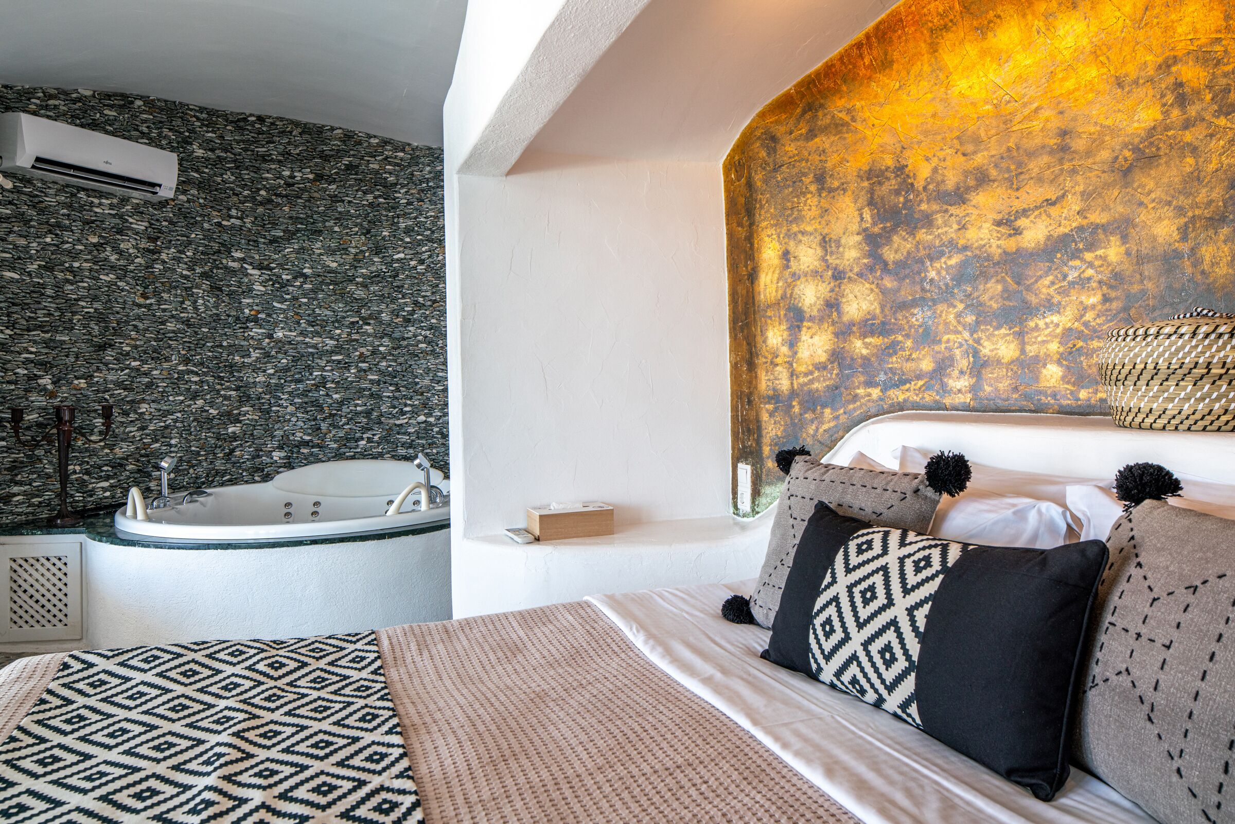 A bedroom with a large bed, a built-in bathtub, and a textured wall.